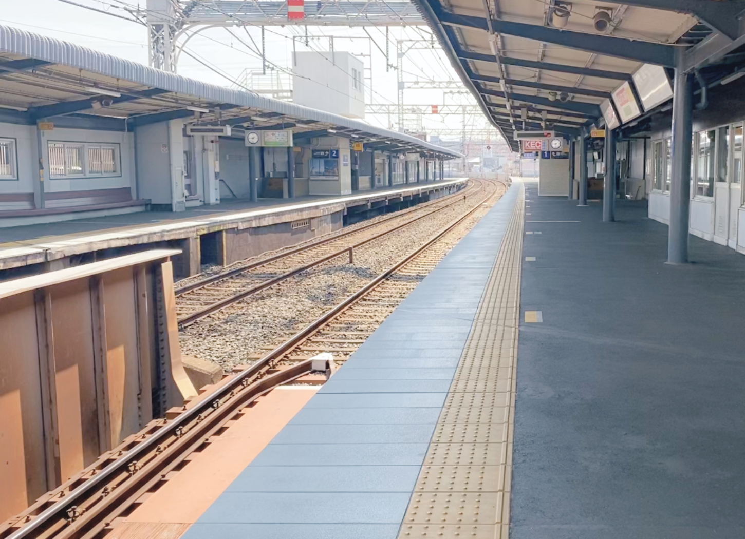 京阪電車牧野駅（大阪府枚方市）のホーム風景。線路が伸び、広告の看板や時計、木製のベンチ、待合室が並んでいる。