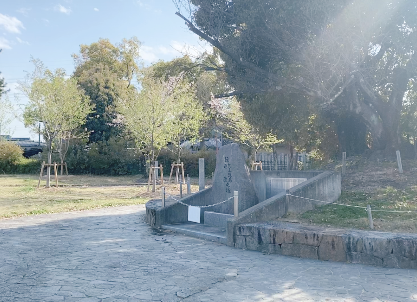 枚方市・牧野公園の大きな石碑。背後に茂る木々と太陽光により石碑が陰影を帯びている風景。