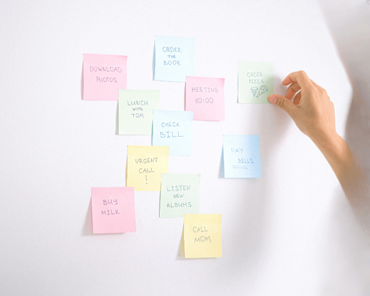白い壁に淡い色の付箋が並び、手が「ToDo」と書かれた付箋に触れている様子