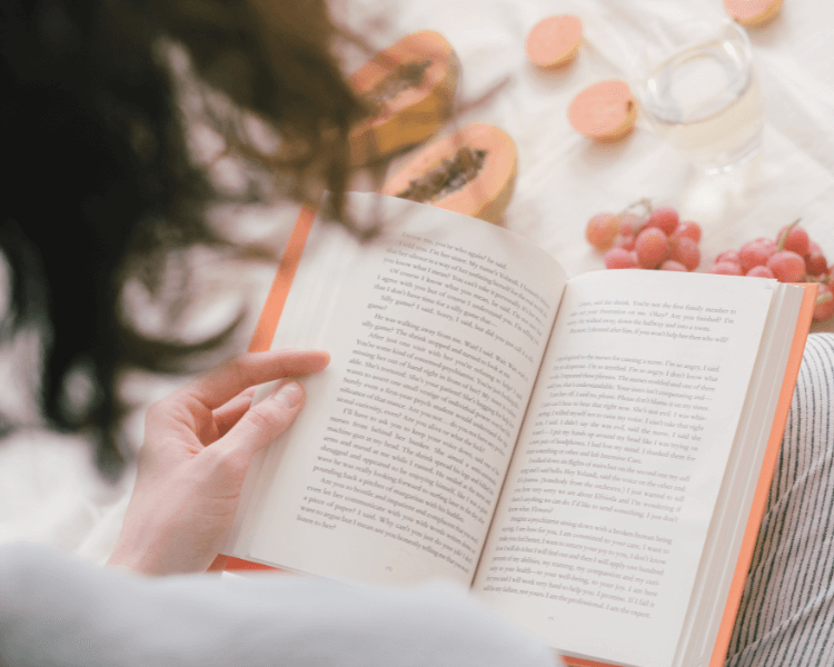果物が置かれたテーブルで、本を読みながら過ごす女性の落ち着いた風景