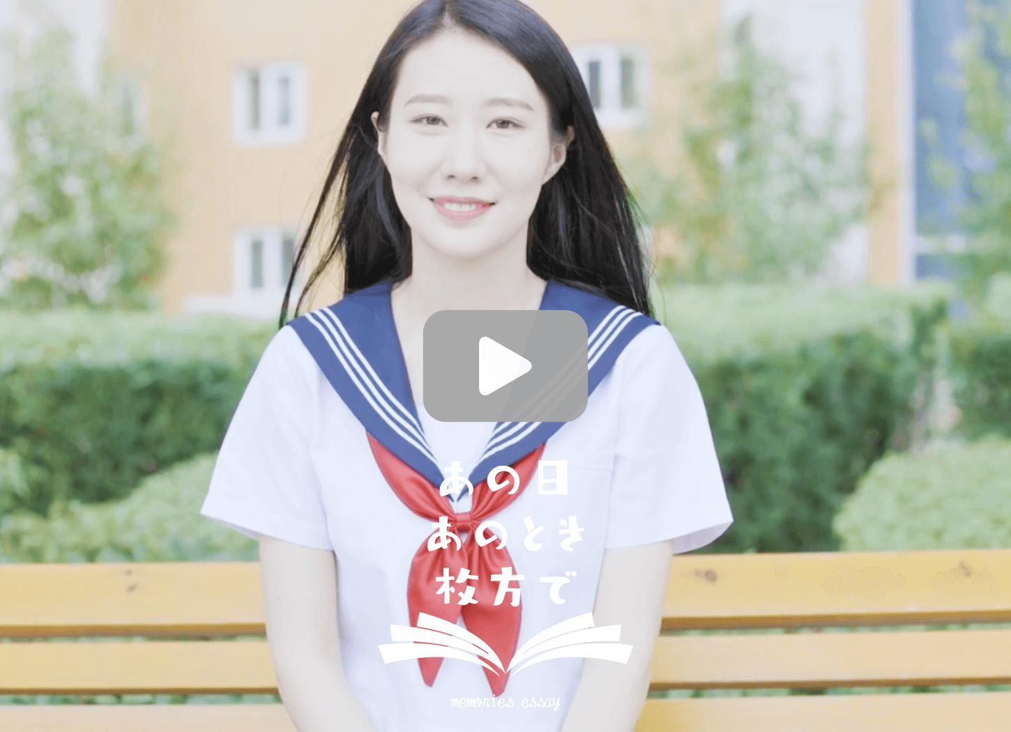 セーラー服を着た長い髪の女の子がベンチに座って微笑んでいる。画像をクリックするとYouTube動画が開く