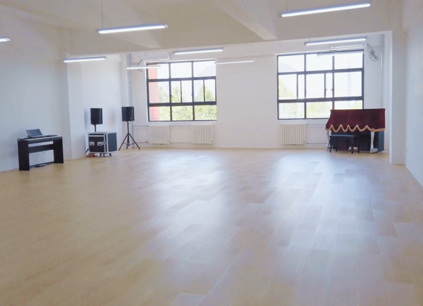 無人の音楽室。木製フロア、右奥にカバーのかかったピアノがあり、窓から外の景色が見える