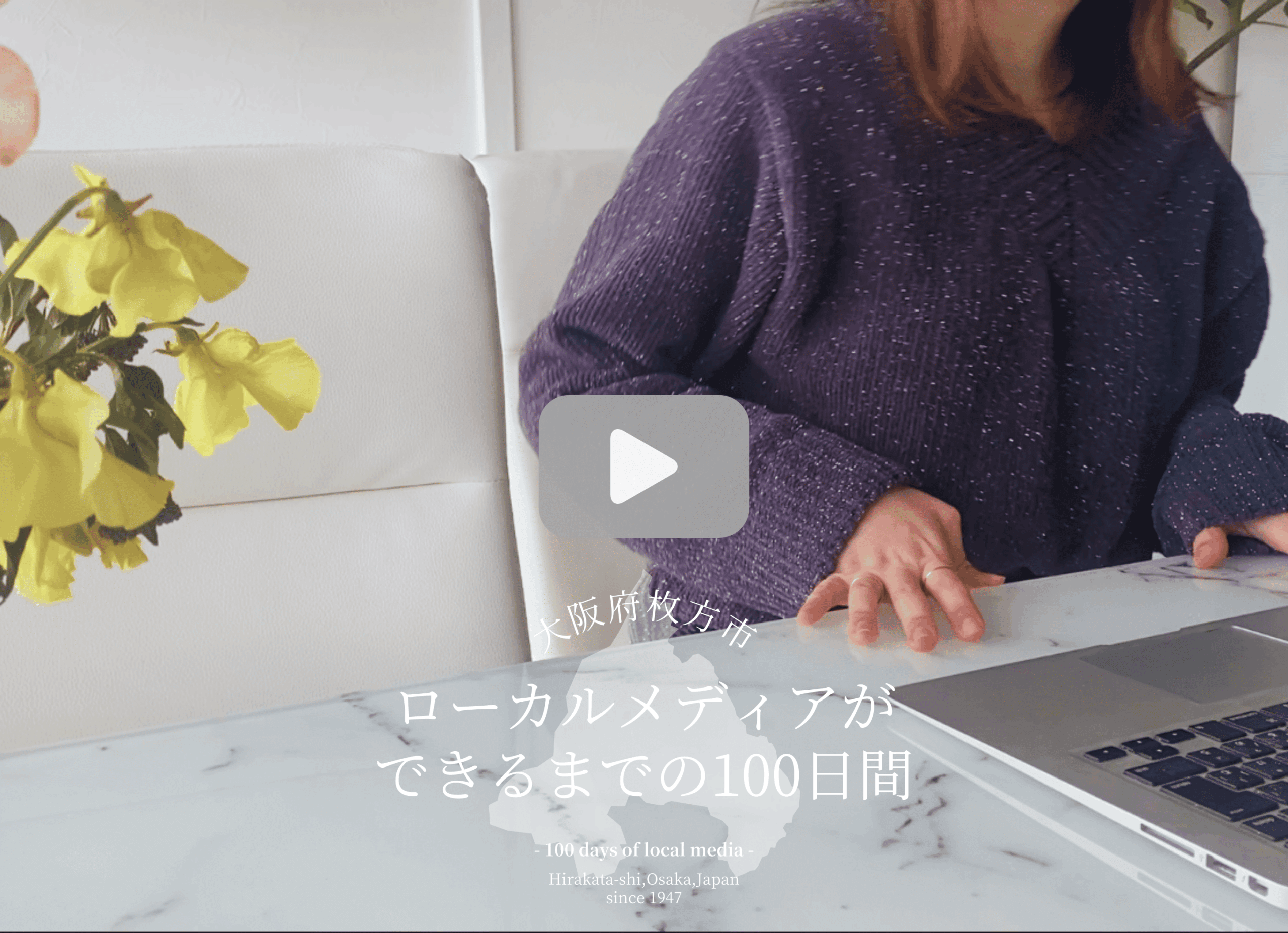 花瓶に生けた花と大理石柄のテーブル、その上のMacノートパソコンと椅子に座る堀寛未。クリックするとYouTube動画が再生されます。