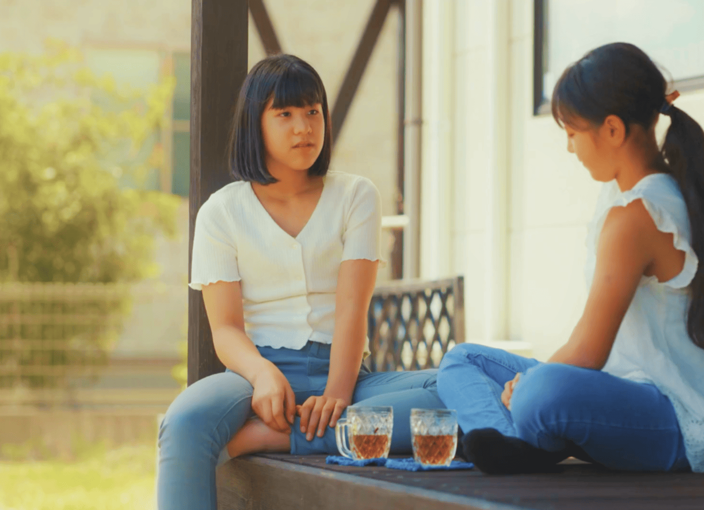 自宅の縁側に座り、お茶を飲みながら会話する二人の女の子。白のトップスにデニムの似たファッションで、二人の「ひろみちゃん」をイメージ。
