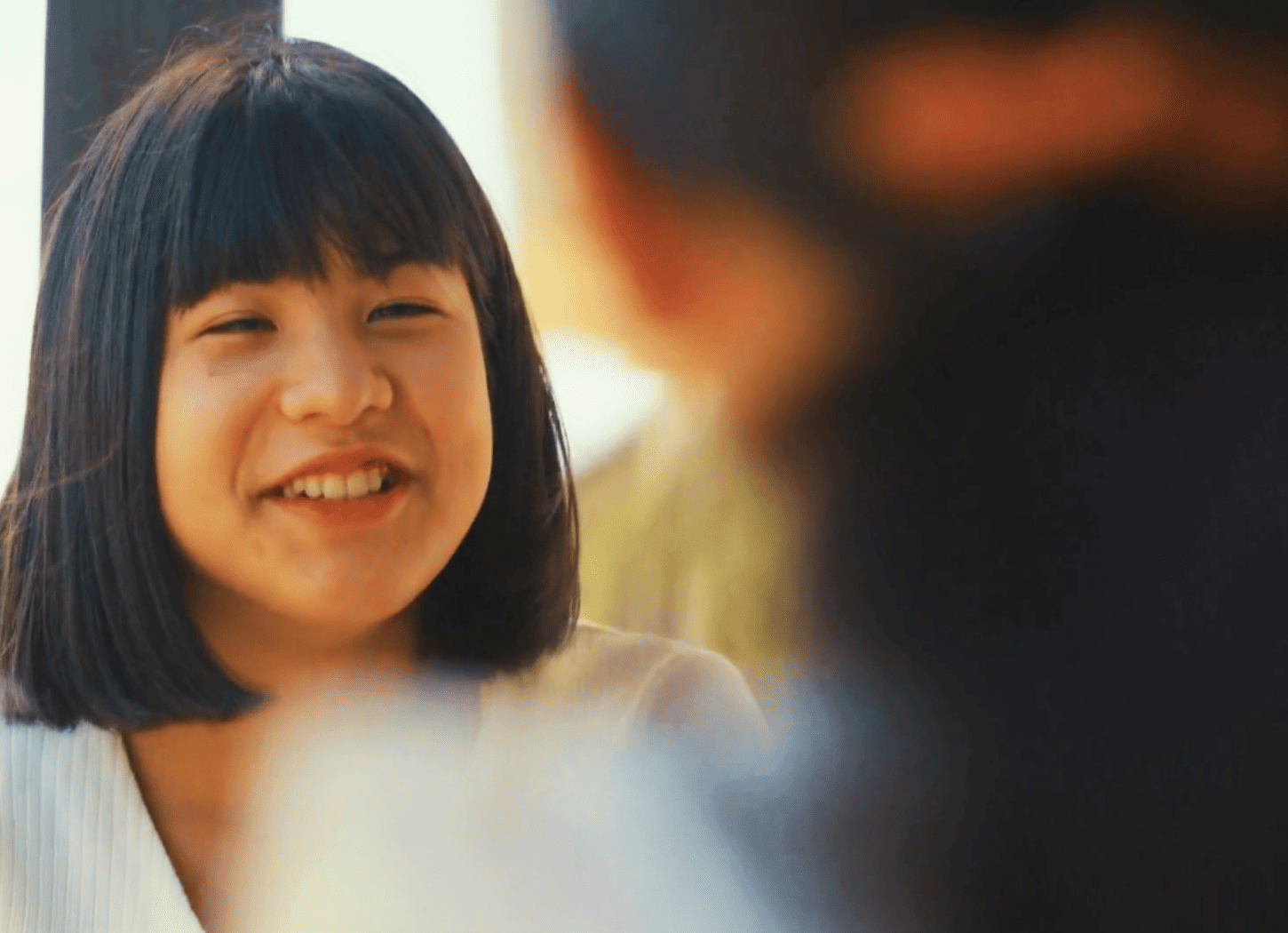 楽しそうに笑うおかっぱの女の子と、向かいに座る髪の長い女の子の背中。二人の「ひろみちゃん」が自宅で楽しそうに会話している様子。