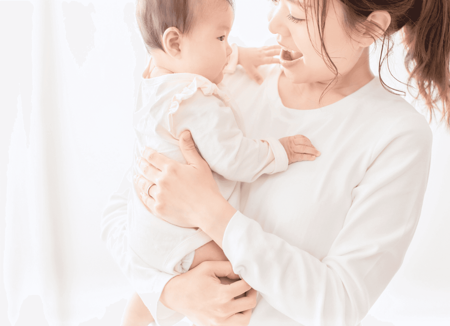 白い服を着たママが赤ちゃんを抱っこして笑顔を見せている様子