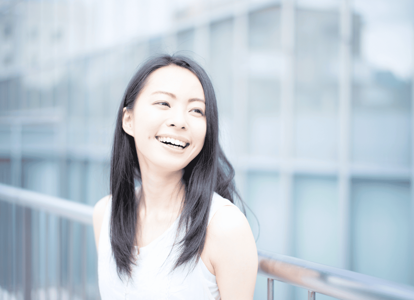 ガラス張りのビルの前で微笑むノースリーブに長い黒髪の女性。Re:HIRAKATAのこれからについて語るイメージ。