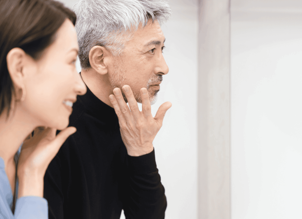 鏡の前で髭を剃る夫をからかう女性