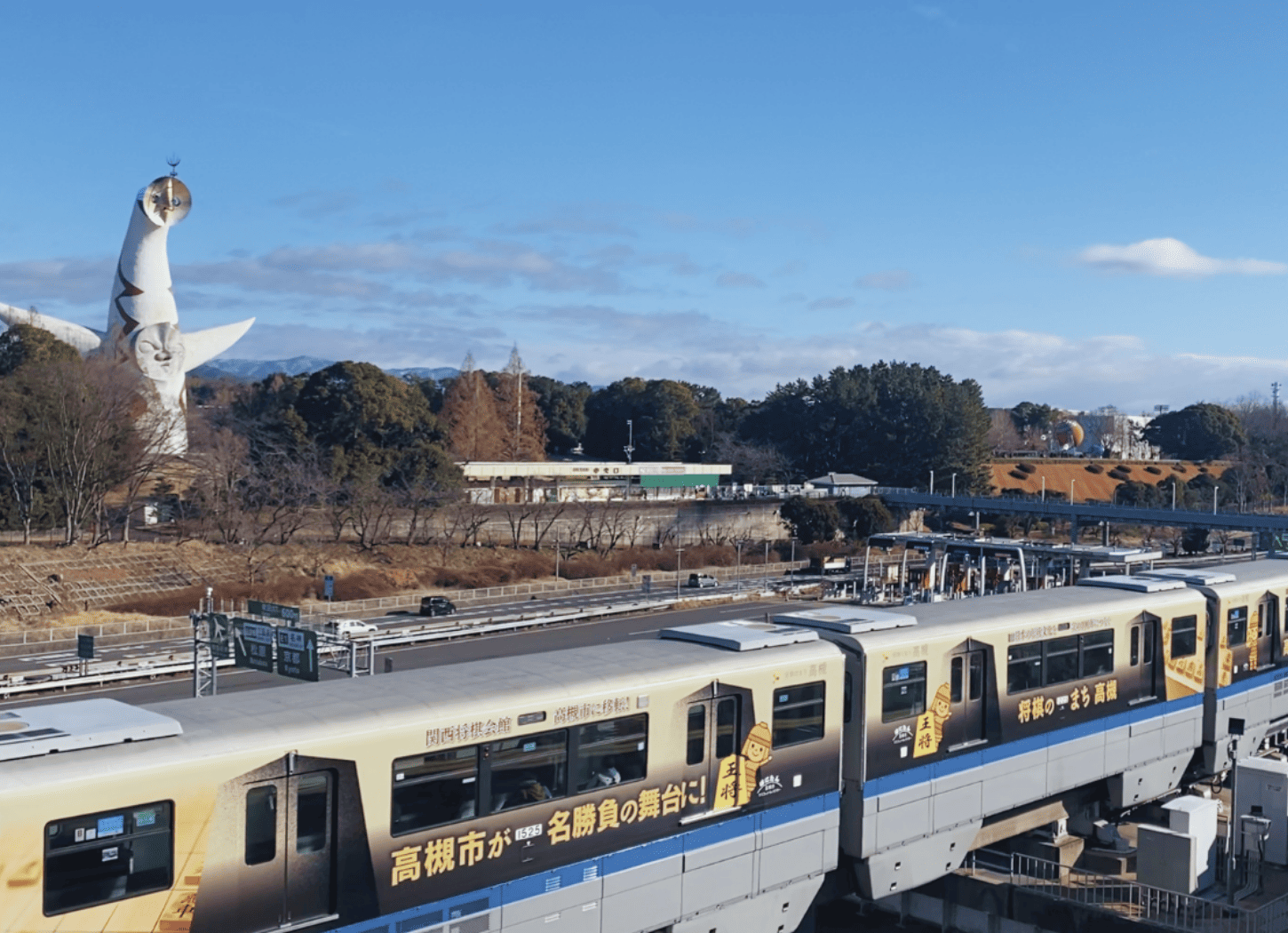 大阪モノレール『万博記念公園駅』を下車し、スロープを降りると左手にモノレールが走る。奥には太陽の塔が見える景色