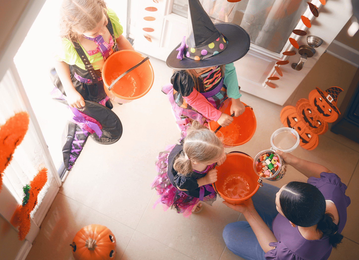 ハロウィンに、魔女の帽子をかぶった子どもたちがオレンジのバケツを手に家を訪れ、お菓子を受け取っている様子