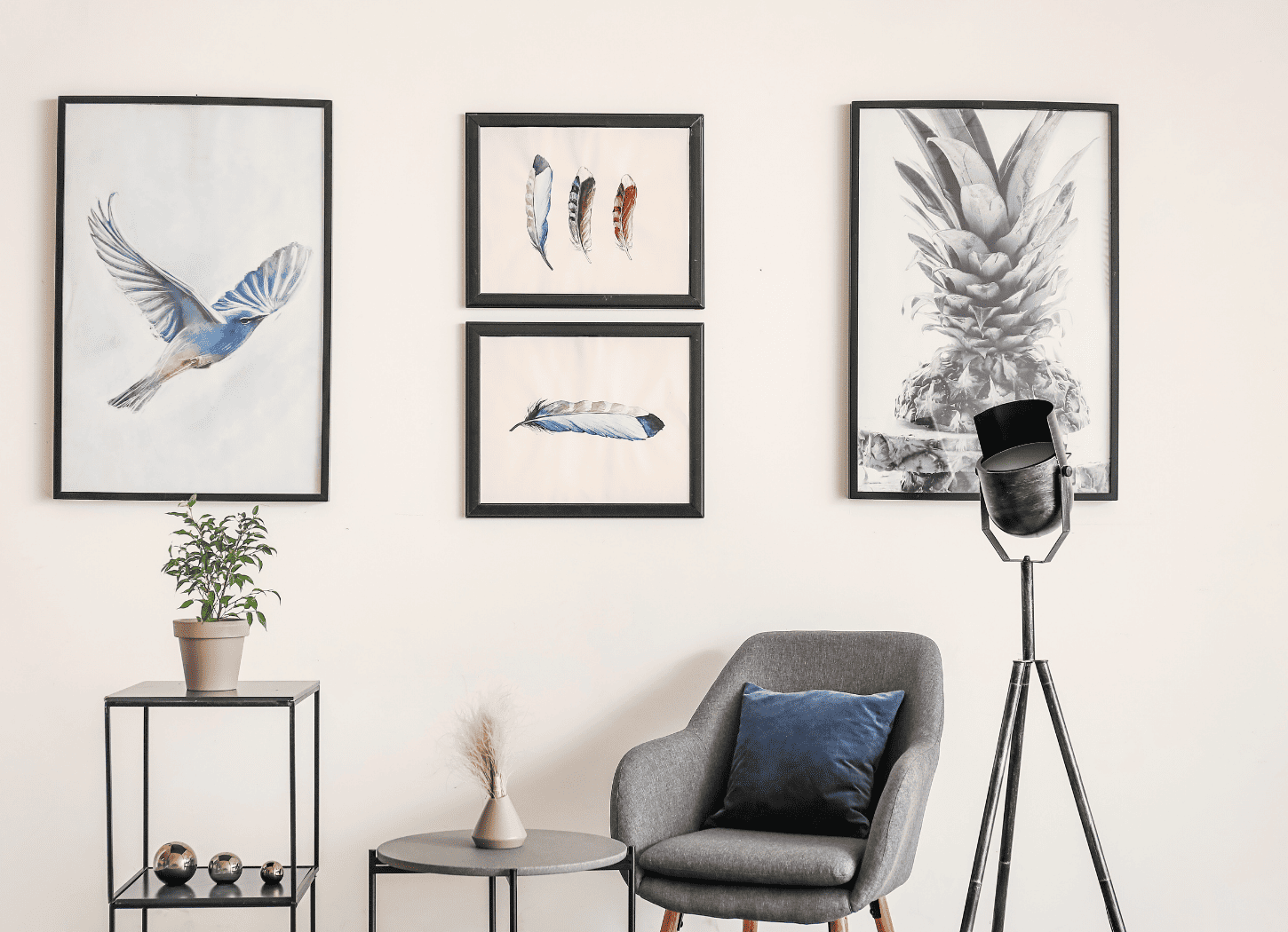 白い壁に黒い額縁の絵が複数飾られている。手前にはグレーの一人掛けソファとブラックのスタンドライト、オブジェや植物を飾った棚が見える。バーチャルイラストレーター星奈がインタビューに答えた部屋をイメージ