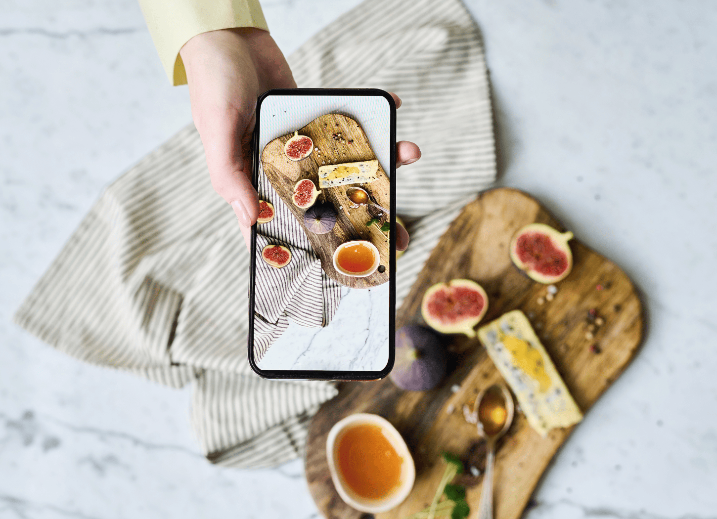 カッティングボードにおしゃれに盛り付けたフルーツをスマホで撮影する女性の手。SNSで他のママの投稿を見る相談者の視点をイメージ。