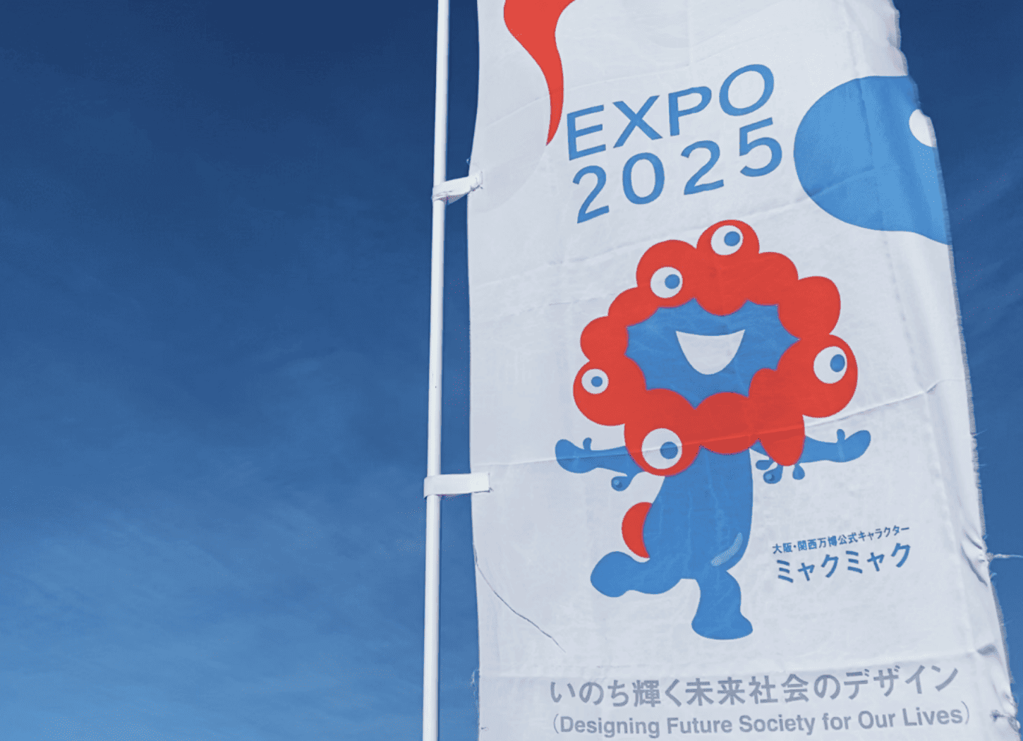 青空の下で風にはためく、白い背景にミャクミャクが描かれたのぼり