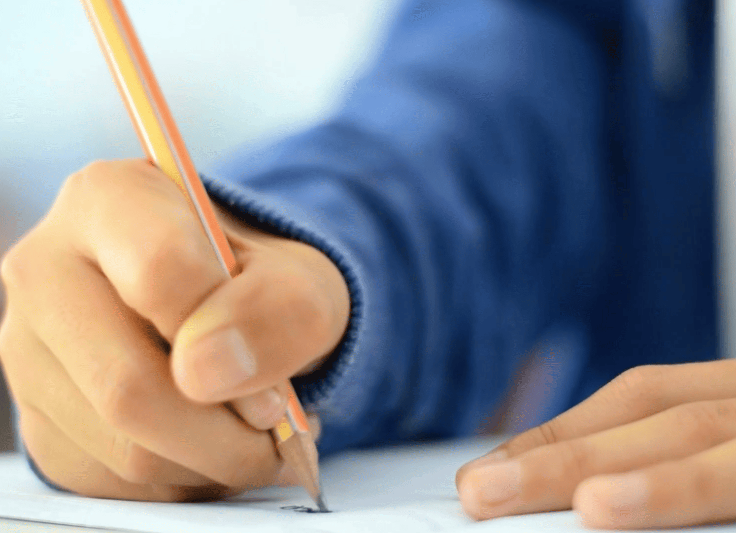 右手に山吹色の鉛筆を持ち、白い紙に文字を書く手元のアップ。中学生のNちゃんのカクカクした個性的な文字と、手紙交換の思い出を象徴するイメージ。
