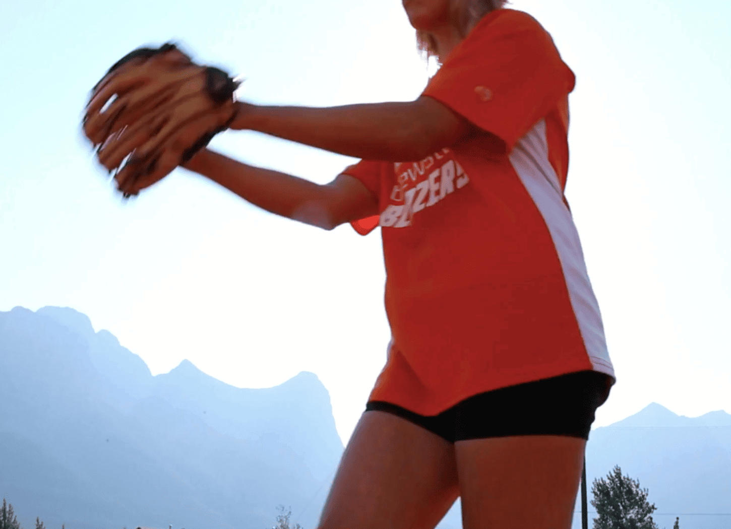 オレンジのユニフォームを着た女の子がグローブをはめ、ボールを投げようとしている。中学生のNちゃんをイメージした元気で明るい青春の一コマ。