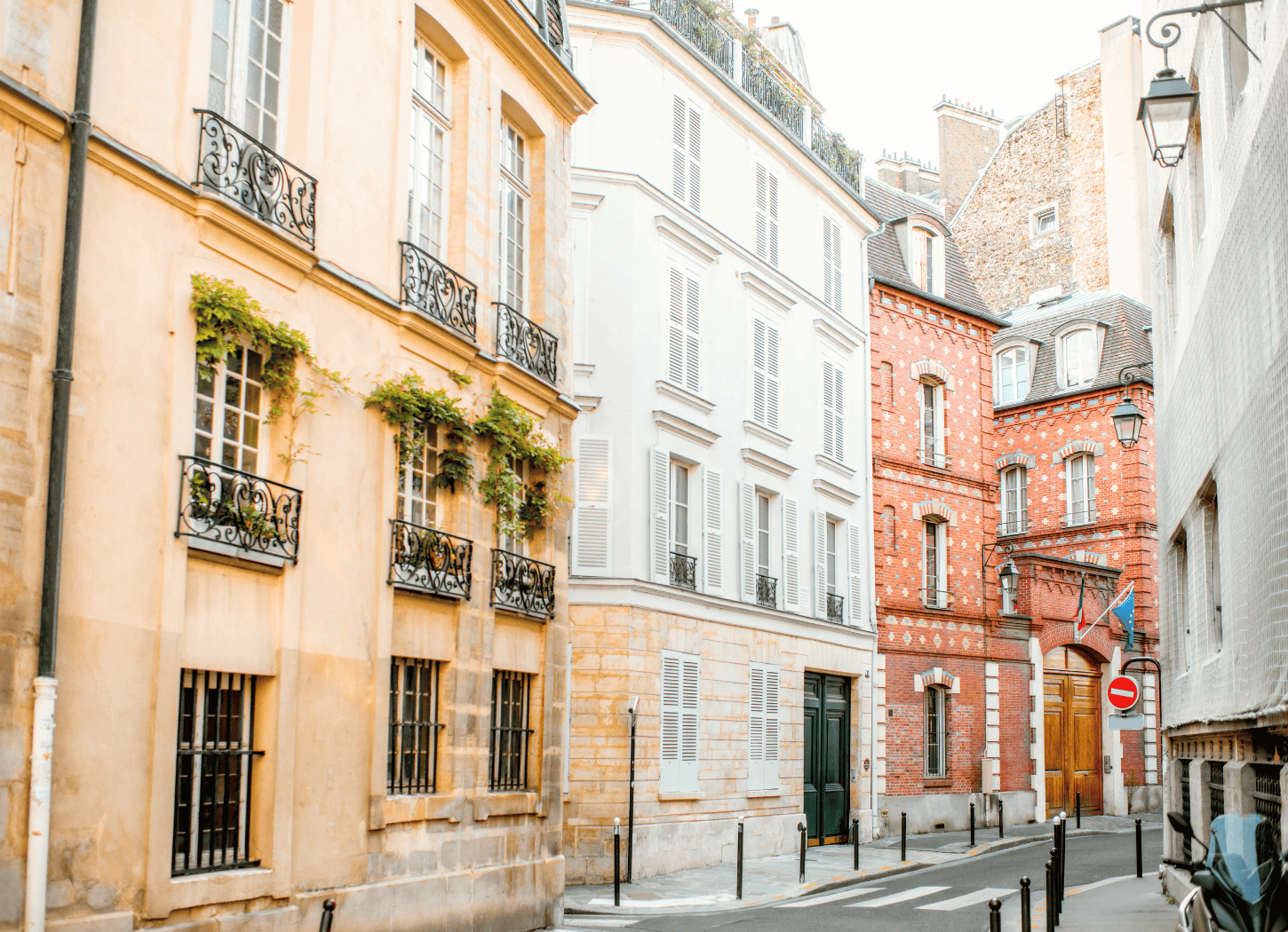 パリの裏路地。薄い黄色やレンガの壁の建物が並び、車や人はおらず静かな街並み。
