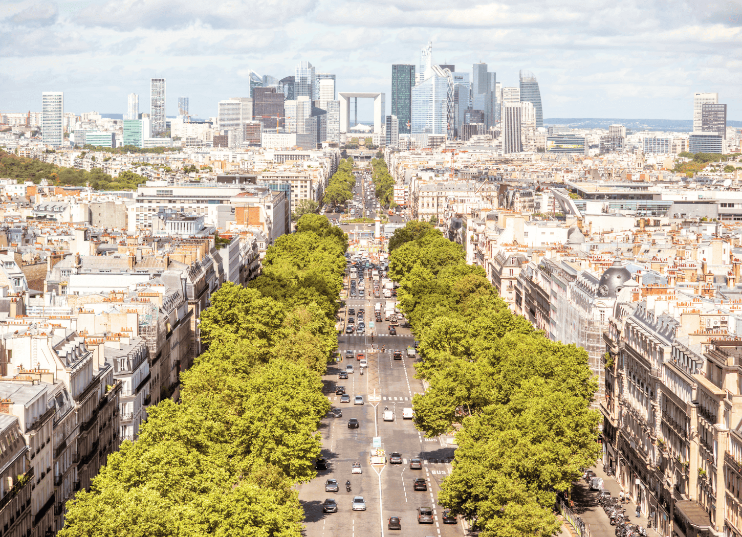 パリのメインストリート。両脇に木が立ち並び、建物が並ぶ街並み。遠くに走る車も小さく見える景観。