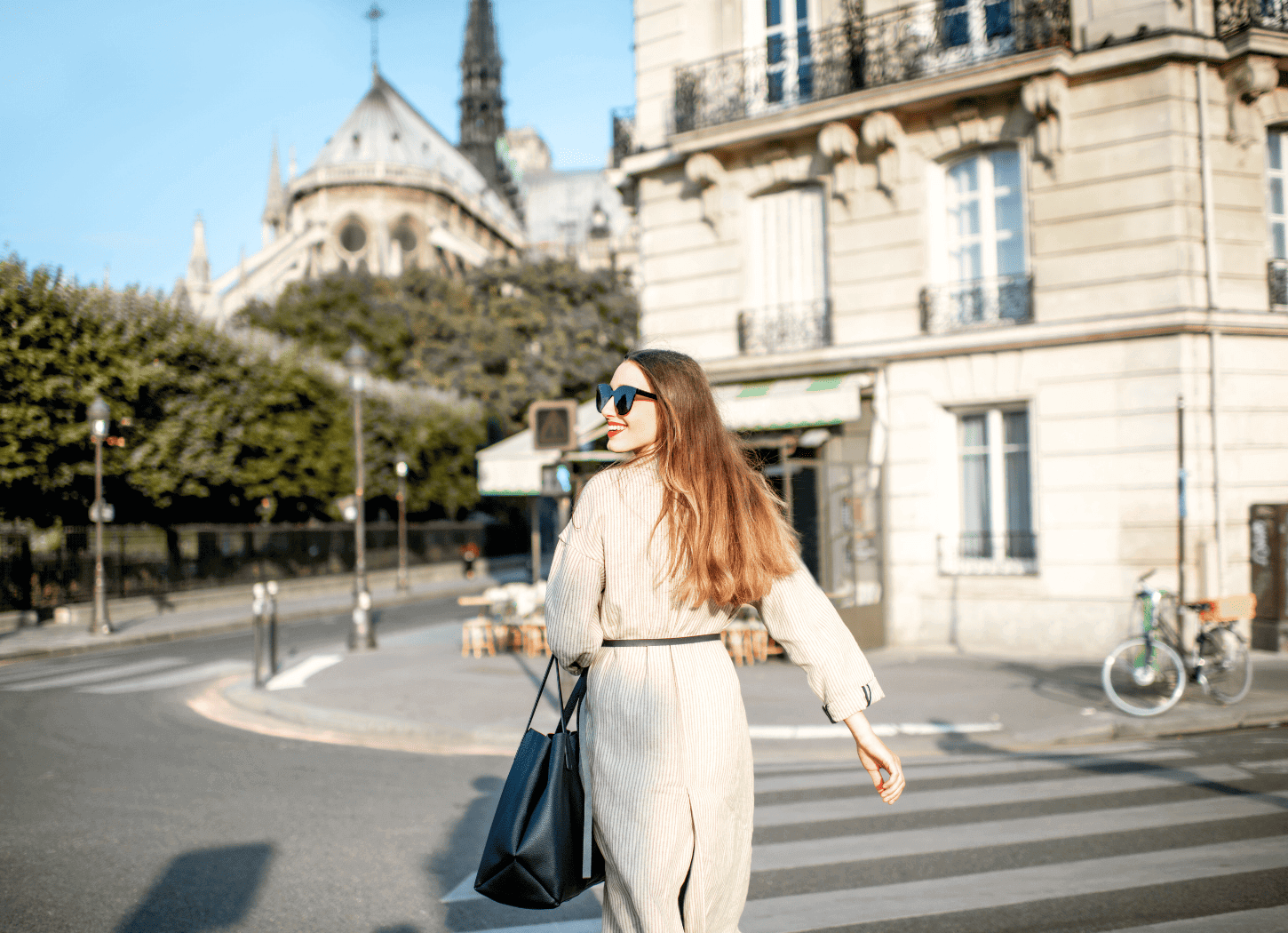 長い髪にサングラスをかけた女性が、パリの街角の横断歩道を渡る後ろ姿。