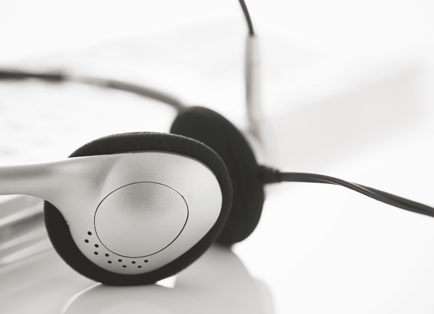 白い机の上に置かれたシルバーの細身のヘッドフォン。奥にはぼやけたパソコンのキーボードが映り、動画編集の一コマをイメージさせる
