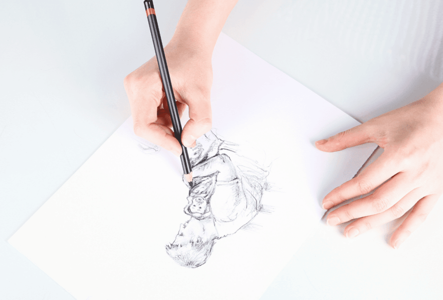 白い机に置いた紙に、鉛筆で絵を描く人物の手元を上から撮影した図。バーチャルイラストレーター星奈が制作している様子をイメージしたカット