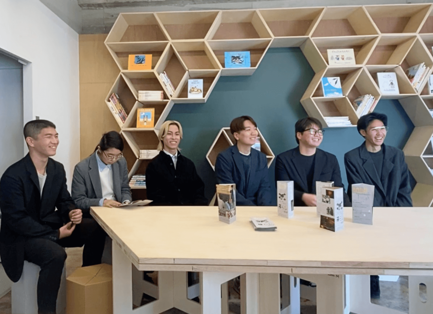 キュウカンサで談笑する大阪電気通信大学の学生たち。背後には黒板と蜂の巣型の本棚に絵本が並んでいる様子