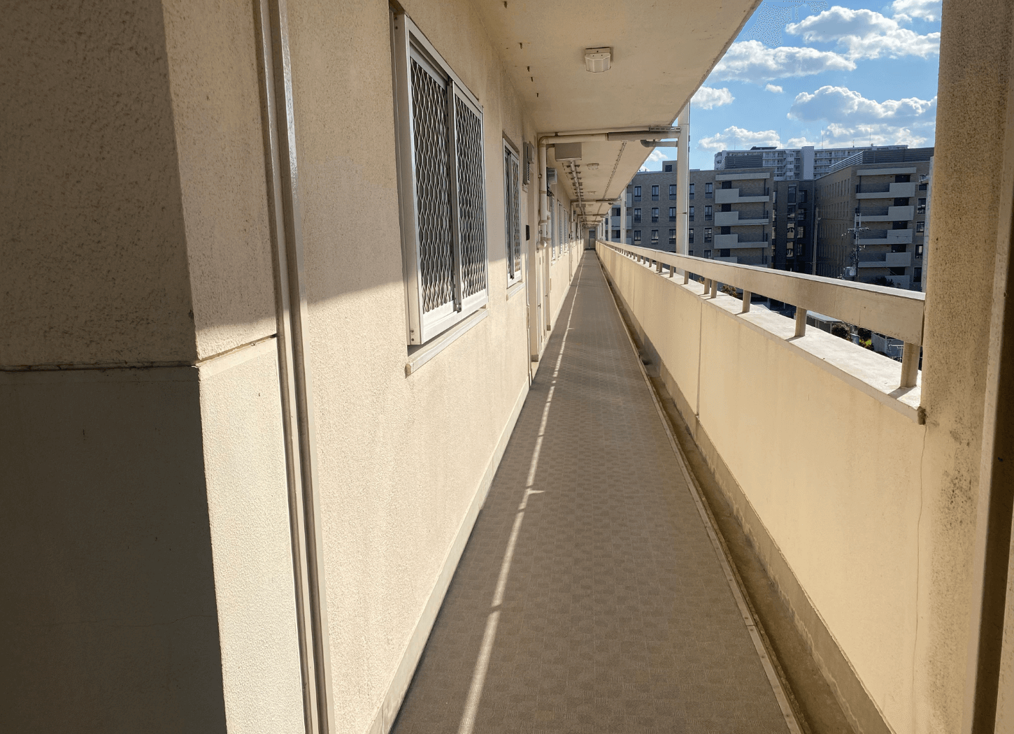 団地の廊下。真っ直ぐに奥まで伸び、太陽の光が差して明るい様子