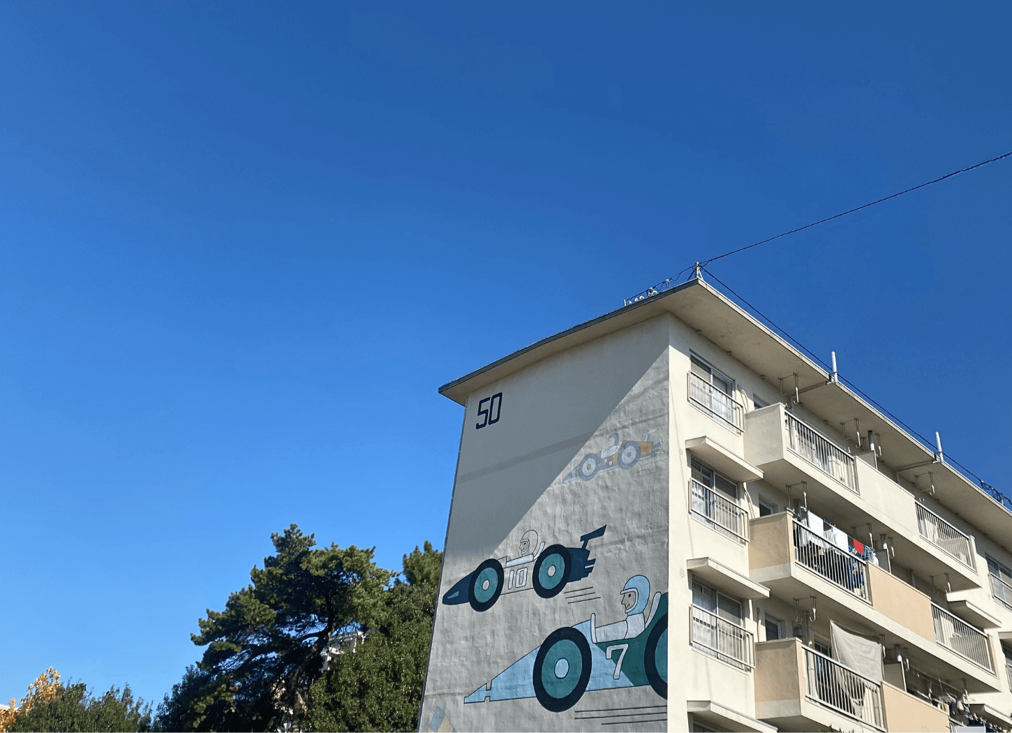 青空の下、中宮第3団地の側面に描かれた「50」の数字とレトロなレーシングカーのイラストを撮影した写真