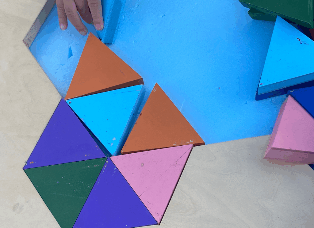 カラフルな三角形のパズルで遊ぶ子どもの手元。いろいろな色を組み合わせて形を作っている様子