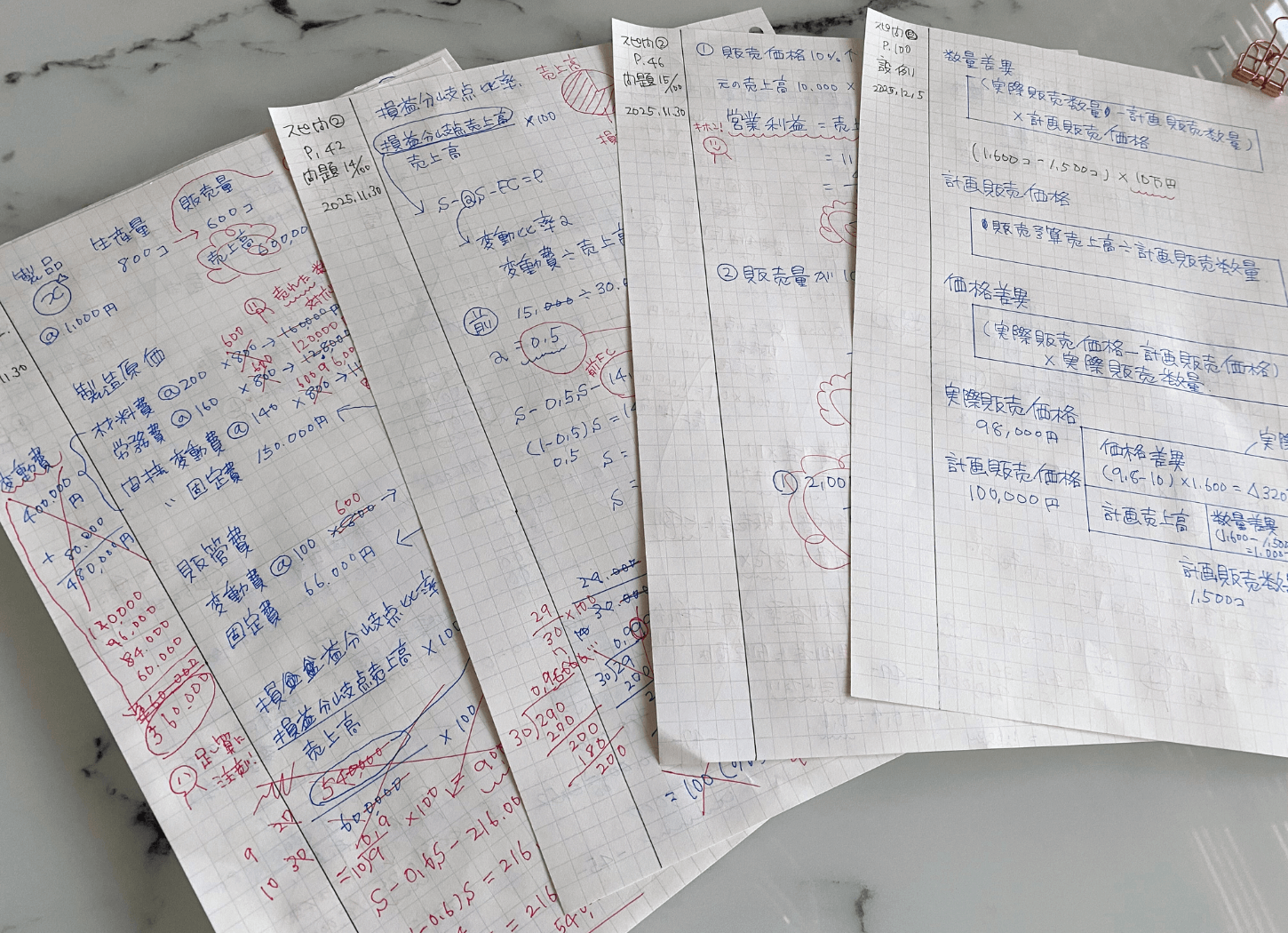 大理石柄のテーブルに広げたルーズリーフに公式や計算式を書き込んだ、中小企業診断士の勉強の様子