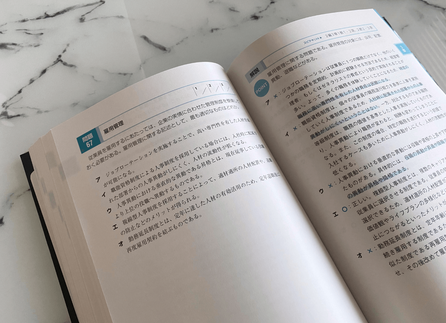 TACのスピード問題集・企業経営理論を開き、雇用管理の問題文と選択肢が左側、解説が右側に掲載されたページをアップで撮影した様子