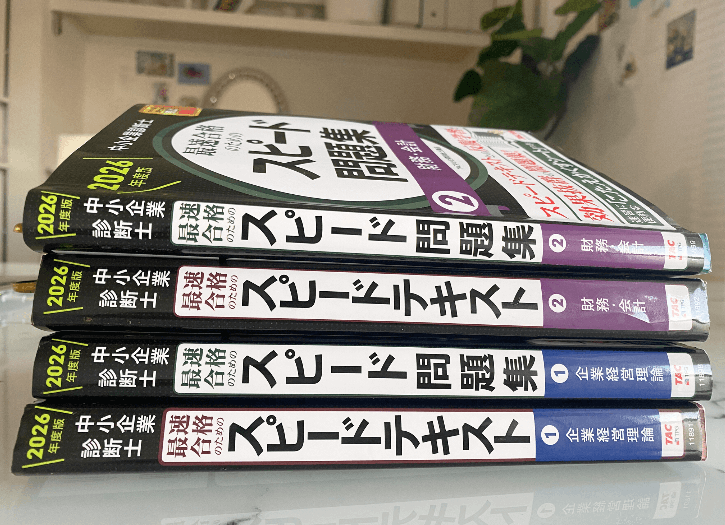 大理石のテーブルの上に、TACのスピードテキストとスピード問題集の企業経営理論・財務会計の4冊が背表紙側から積み上げられている様子。厚みから学習範囲の広さが伝わる