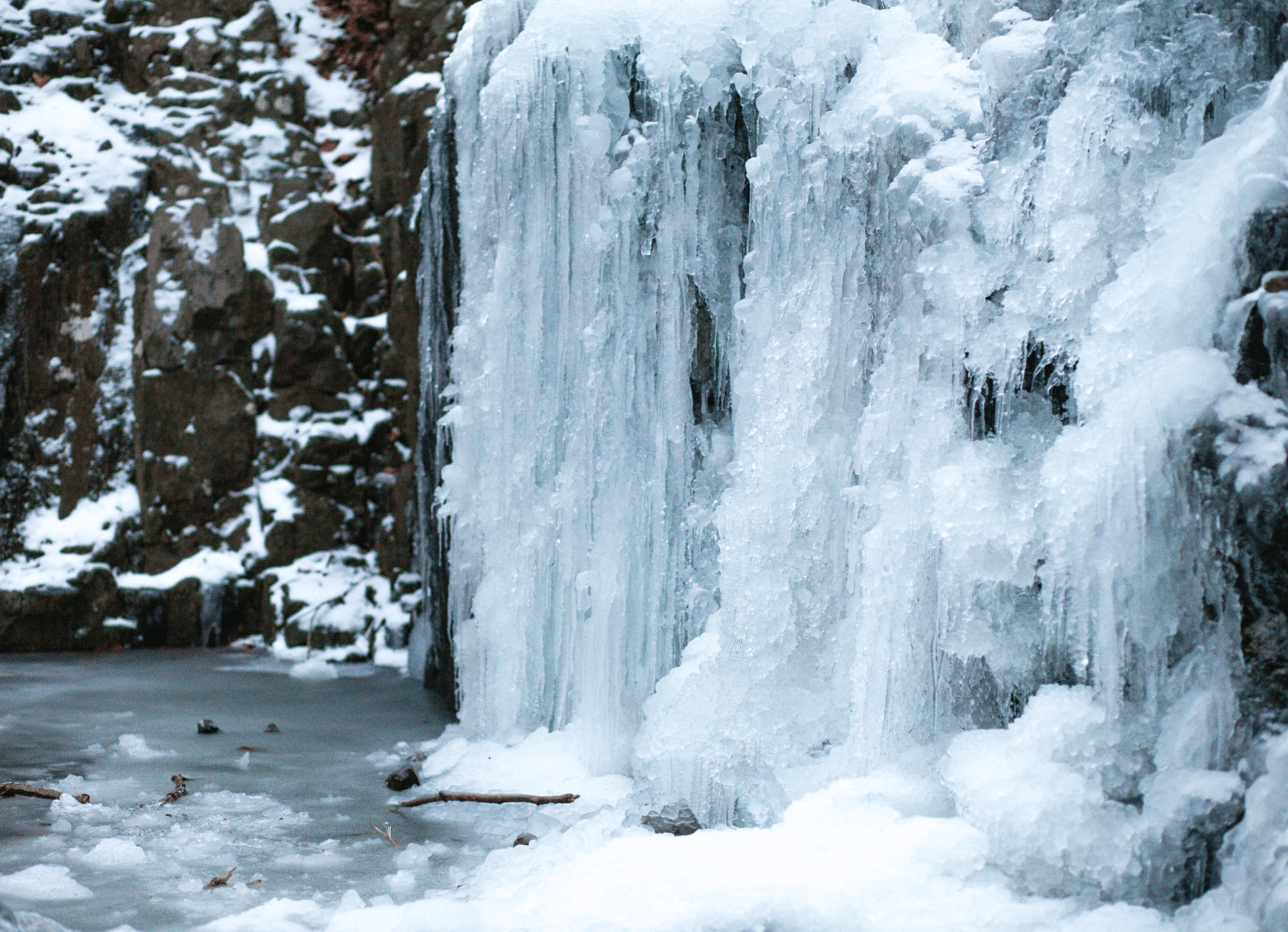 黒い岩に雪が積もり、横から見た小さな滝が凍りついている水沢腹堅の風景