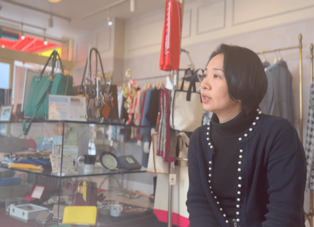 紺のジャケットにパールをあしらった奥様が椅子に座り、富江さんと会話する横顔。de lusso店内での取材風景