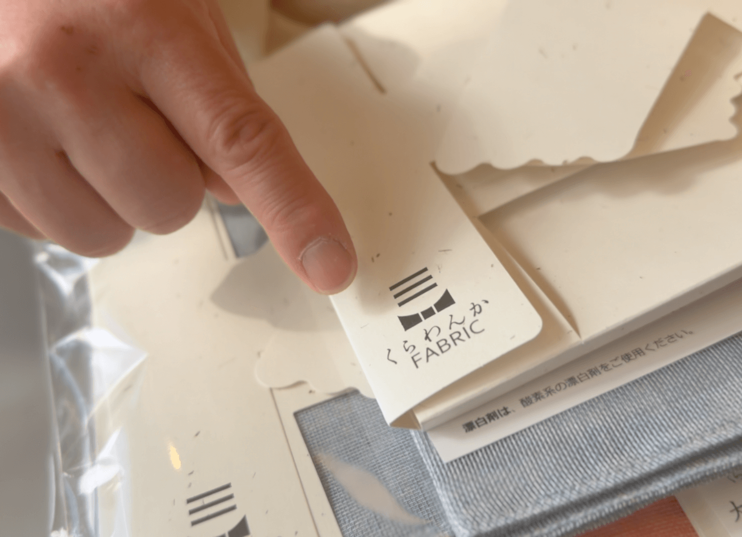 くらわんかファブリックのロゴを指し示し説明する富江さん。三本線は三方よしを表すヨシ、下部には蝶ネクタイをイメージした舟のデザイン