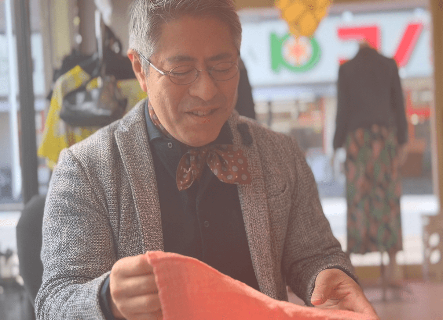 くらわんかファブリックのヨシおてふきん(ピンク)を手に、穏やかな笑顔で話す富江さん。少し伏し目がちな表情の取材風景