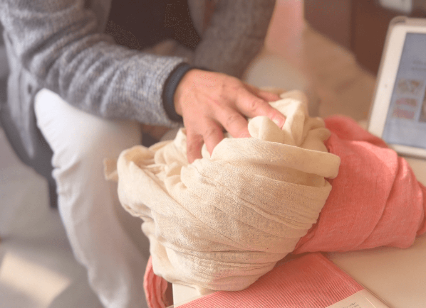 ヨシ素材で作られたくらわんかファブリックの大判生地に触れる富江さん。マフラーやカーテンとして使えるやわらかな質感を伝える様子