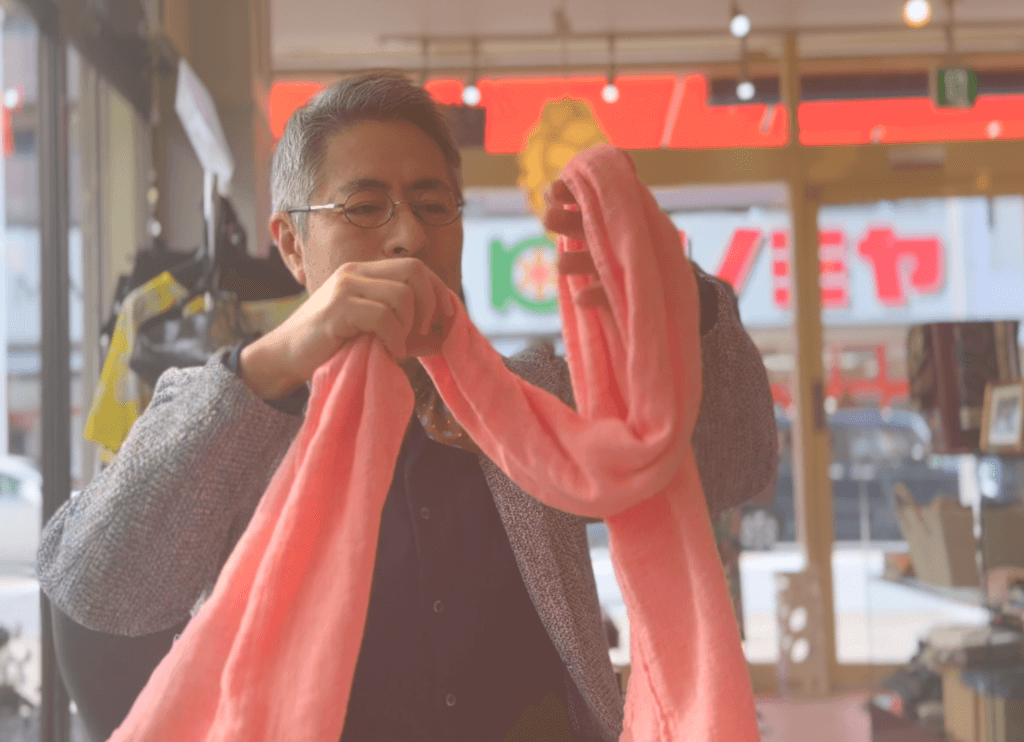 くらわんかファブリックのヨシ素材ストール(ピンク色)を手に持ち、巻く仕草を見せる富江さん。軽やかな質感が伝わる取材風景