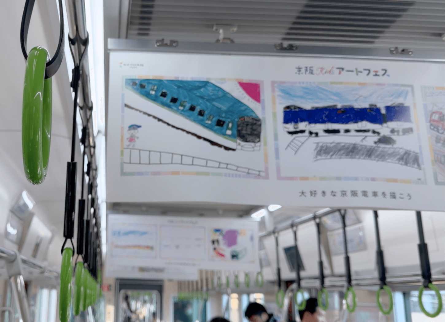 京阪Kidsアートフェストレインの車内。手前で揺れる吊り革の奥に、第4回京阪Kidsアートフェスの子どもたちの作品が展示されている様子。