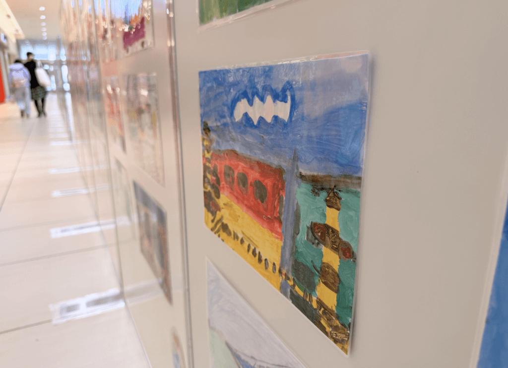 くずはモールSANZEN-HIROBAで展示された第4回京阪Kidsアートフェスの作品。青空が大きく描かれ、踏切と京阪電車の車両が印象的なイラスト。