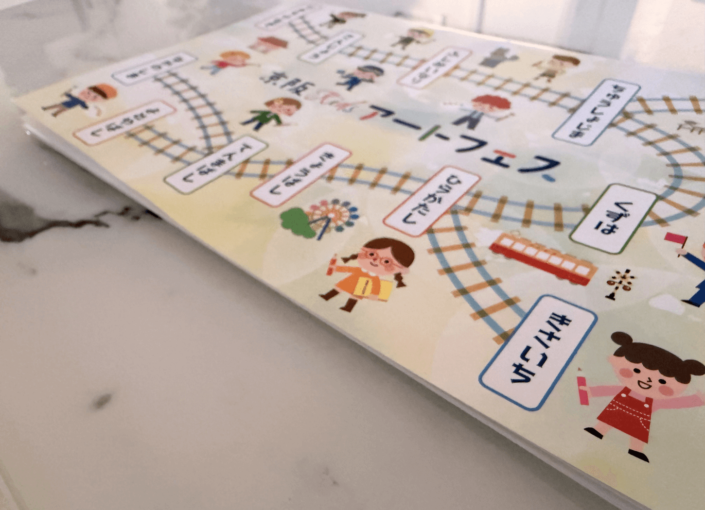 第4回京阪Kidsアートフェスの応募者全員に配布された特製ノートの表紙。京阪電車の路線図と駅名、運転士や画材を持った子どもたちのイラストが描かれている。