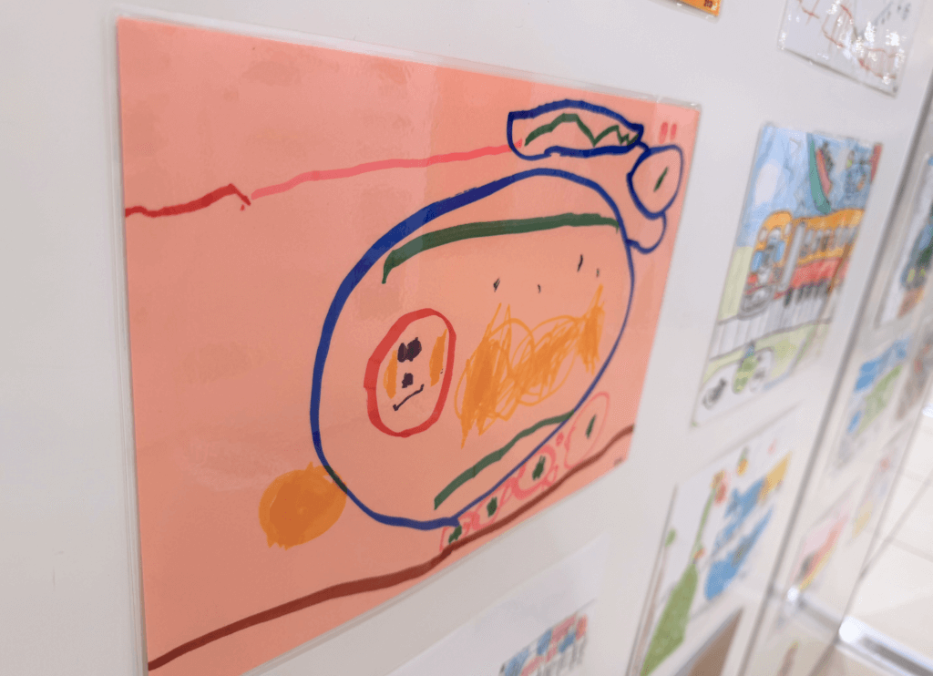 くずはモールSANZEN-HIROBAで展示された第4回京阪Kidsアートフェスの作品。ピンクの色画用紙に青や赤、緑のペンで大胆に描かれた京阪電車のイラスト。