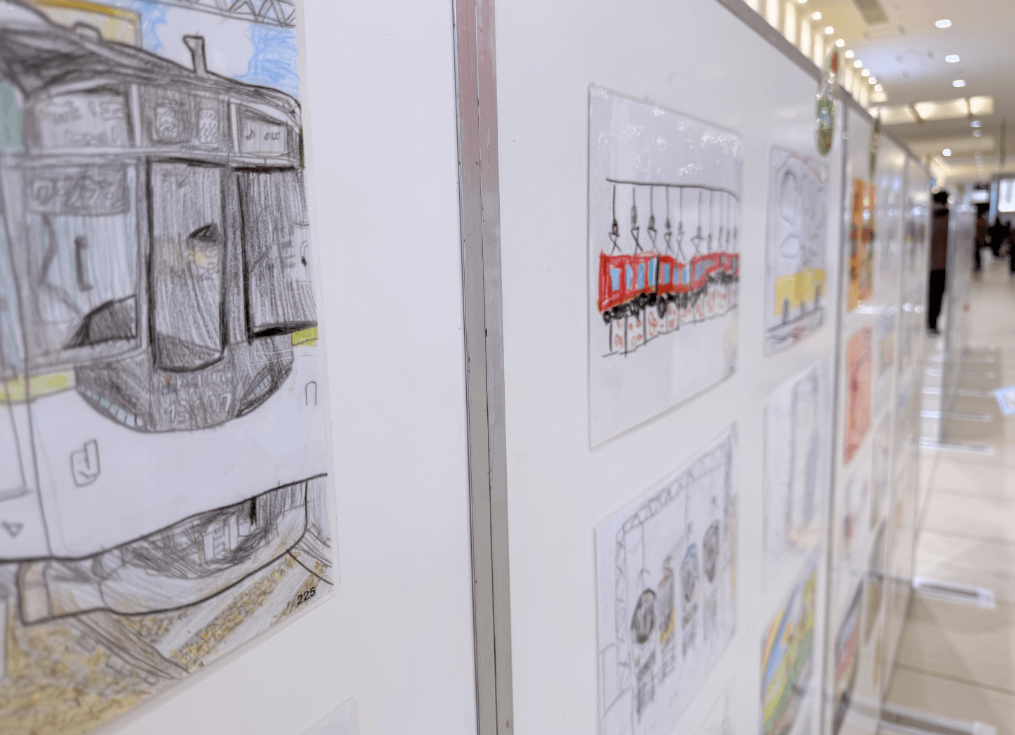 くずはモールSANZEN-HIROBAで開催された第4回京阪Kidsアートフェスの作品展示。手前に運転士が描かれた京阪電車の正面イラストがあり、奥にも子どもたちの作品が並んでいる。