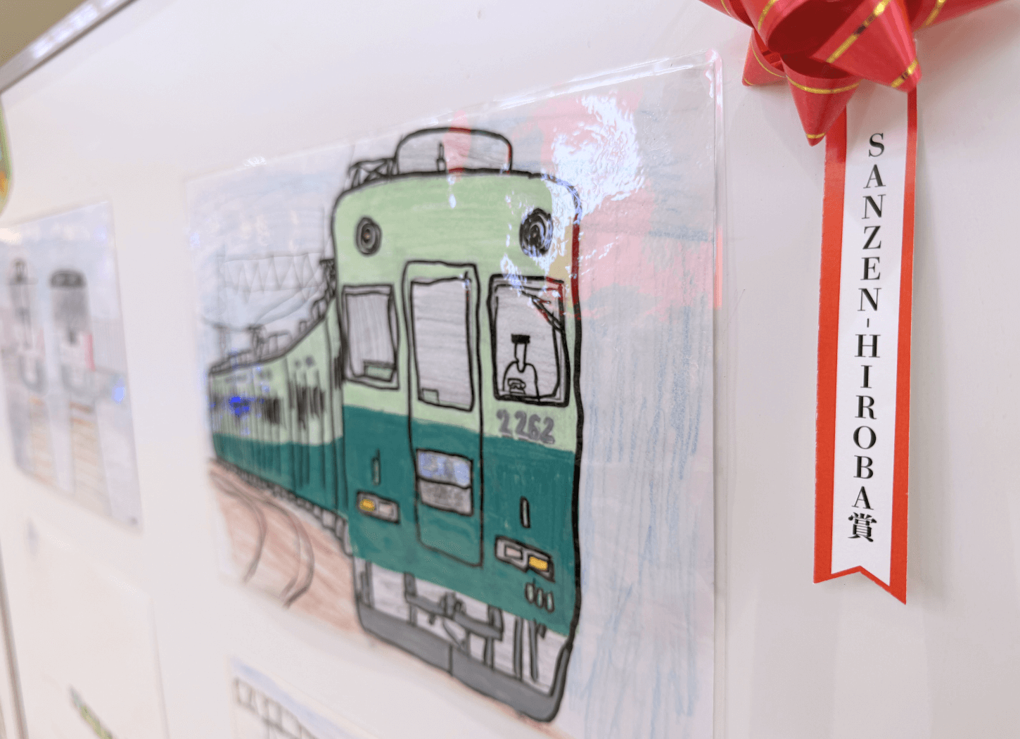 くずはモールSANZEN-HIROBAで展示された第4回京阪Kidsアートフェスの受賞作品。「SANZEN-HIROBA賞」と書かれた赤いリボンが付いた、カーブする線路を走る京阪電車のイラスト。