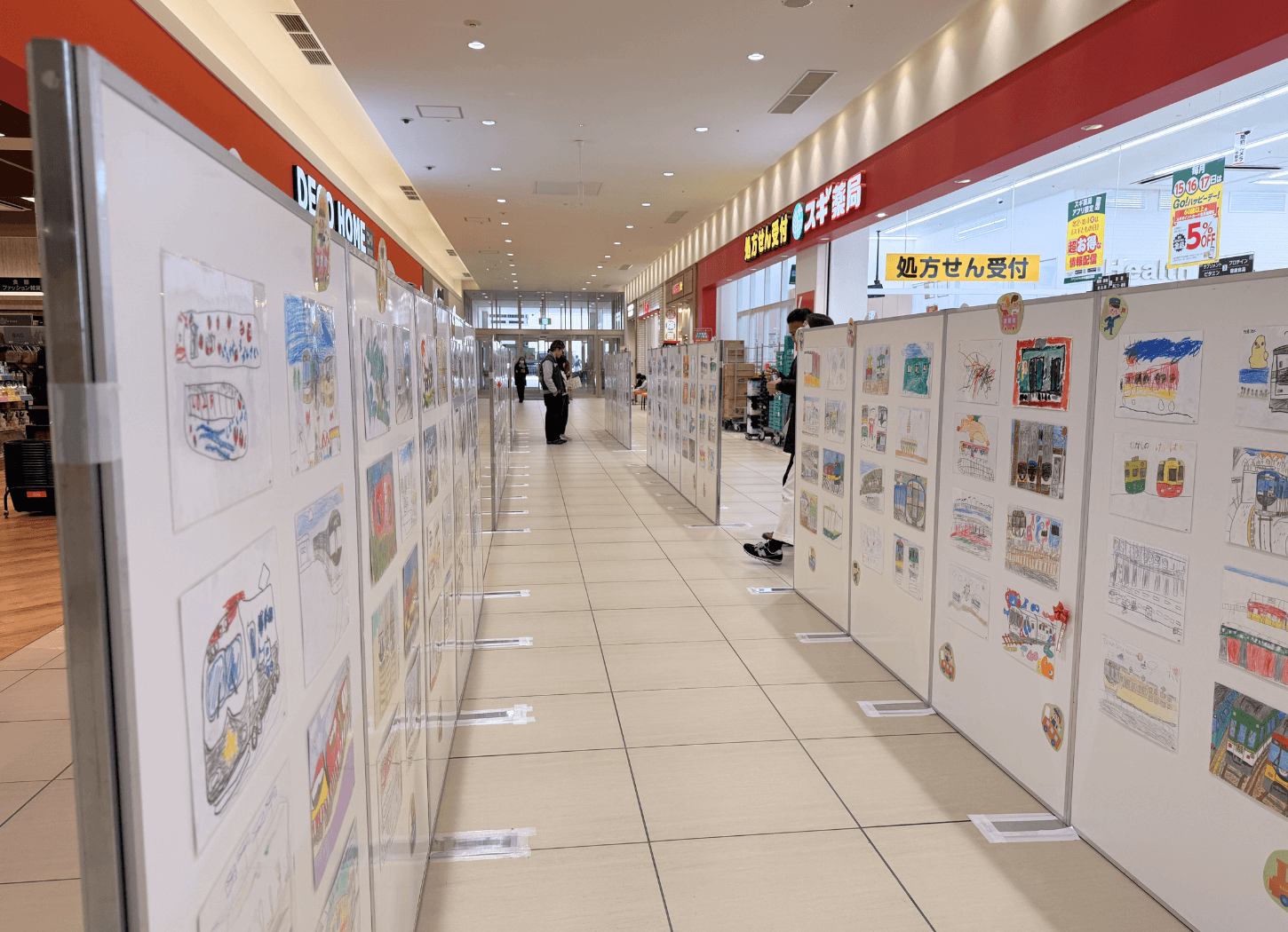 くずはモールSANZEN-HIROBAの通路に並ぶ展示パネル。第4回京阪Kidsアートフェスの子どもたちの原画が2列に展示されている様子。