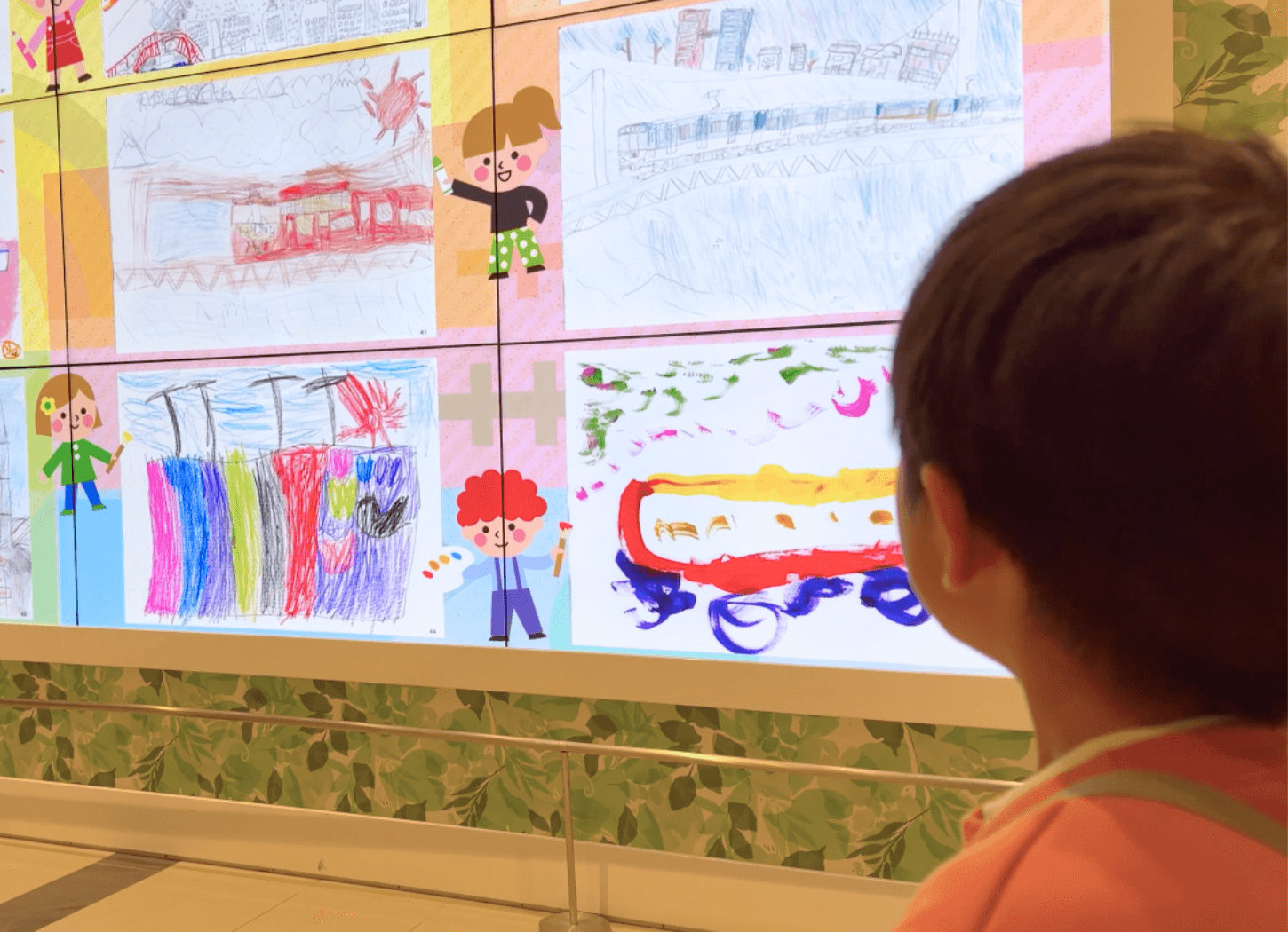 くずはモールSANZEN-HIROBAの大型スクリーンに映し出された第4回京阪Kidsアートフェスの作品を、来場した子どもが見つめている様子。