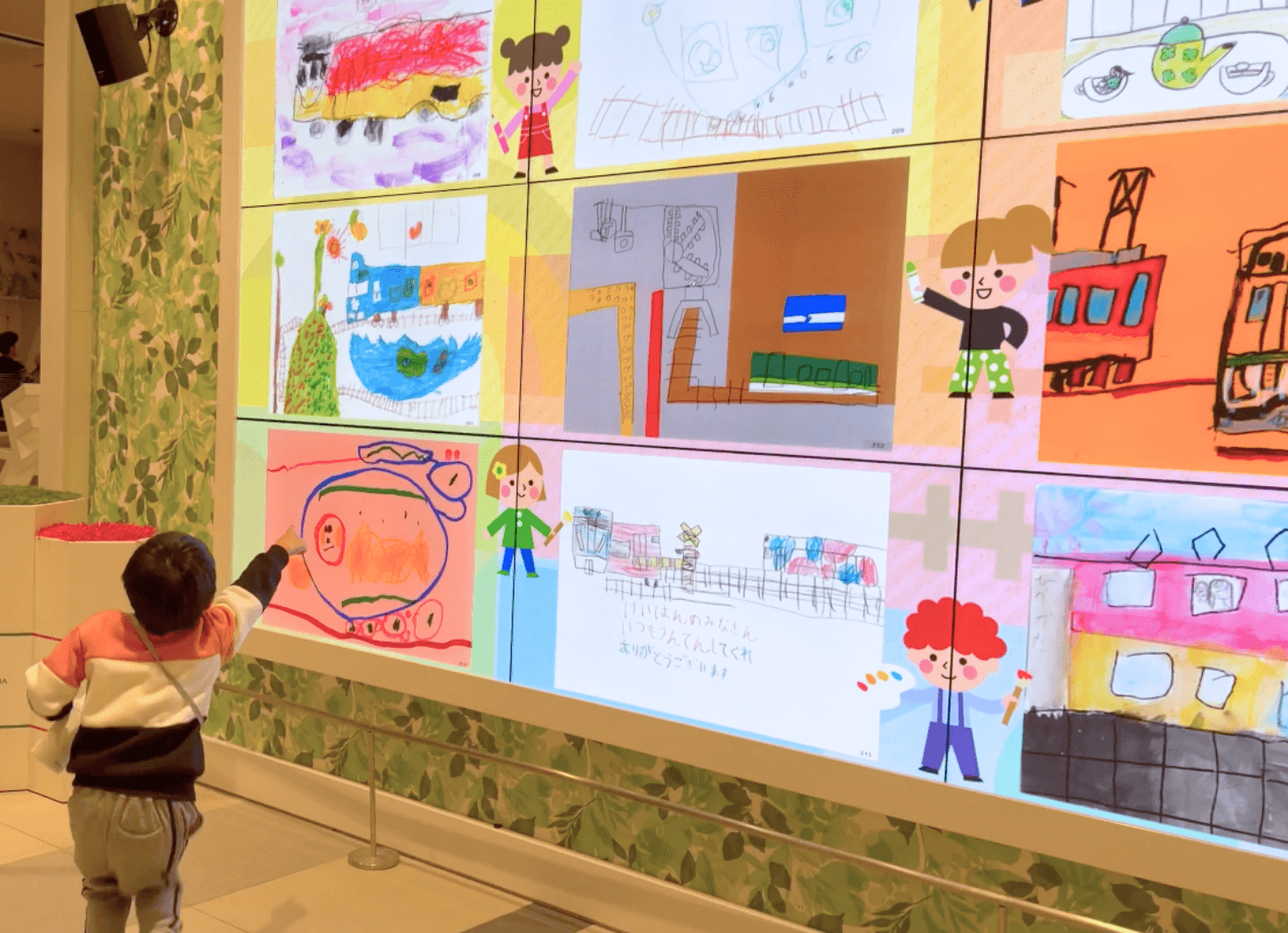 くずはモールSANZEN-HIROBAの大型スクリーンに映し出された第4回京阪Kidsアートフェスの作品を見つけ、指を差して近づく子どもの後ろ姿。