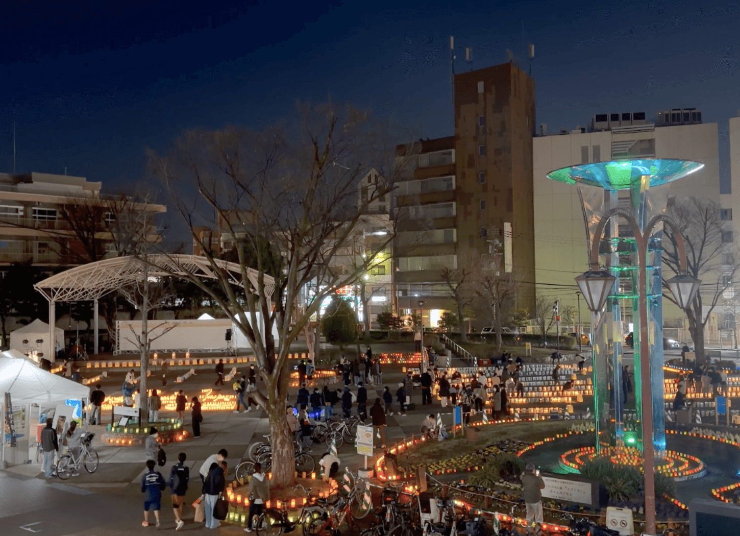 歩道橋から見た夜のニッペパーク岡東中央で、キャンドルが灯るなか人々がゆっくり歩いている様子