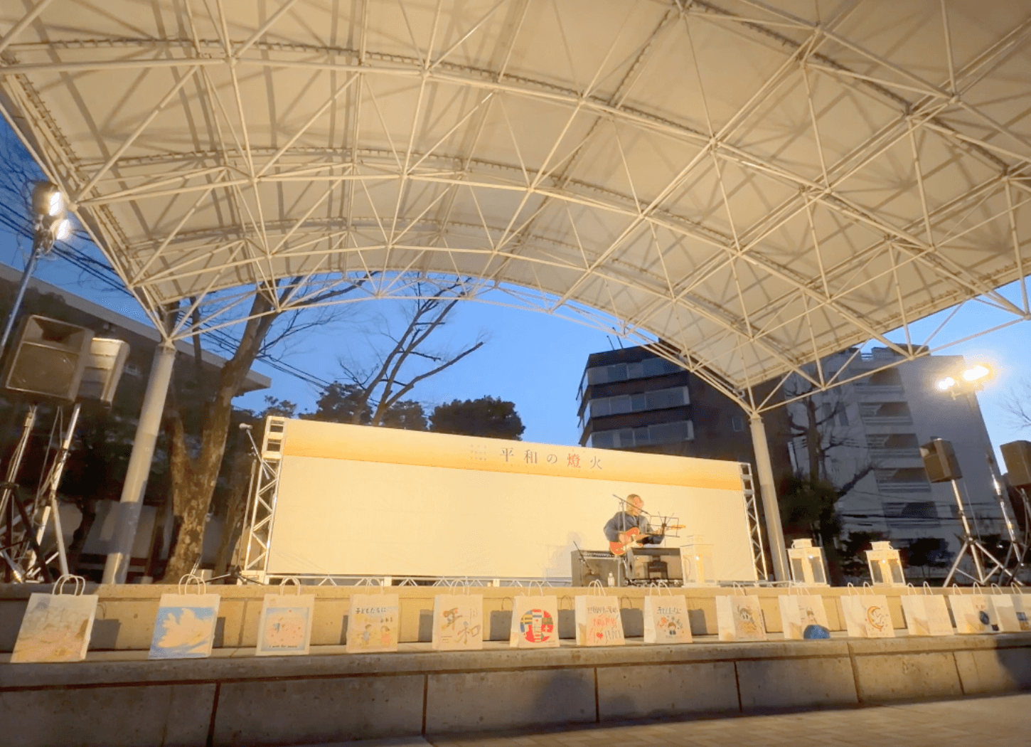 ニッペパーク岡東中央の野外ステージで男性が弾き語りを行い、手前にキャンドルが並んでいる様子