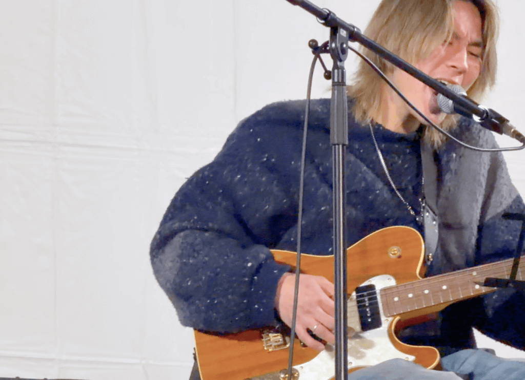 ニッペパーク岡東中央の野外ステージで男性が弾き語りをする様子を近くから撮影した写真