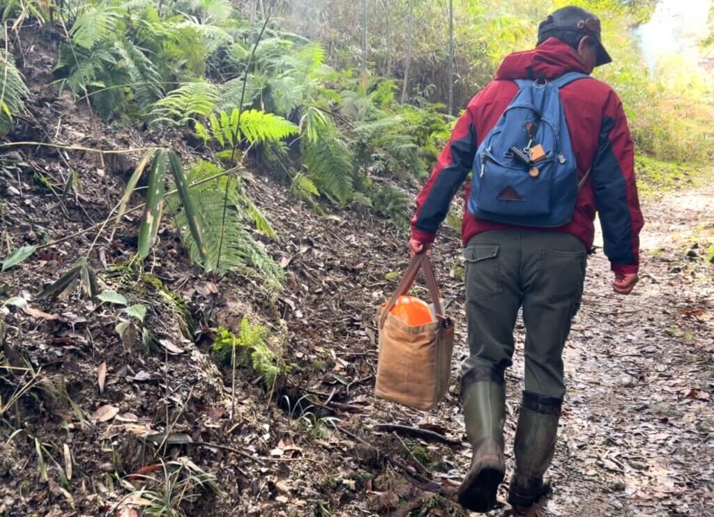 穂谷の里山の道を、道具を手に歩く石野さんの後ろ姿